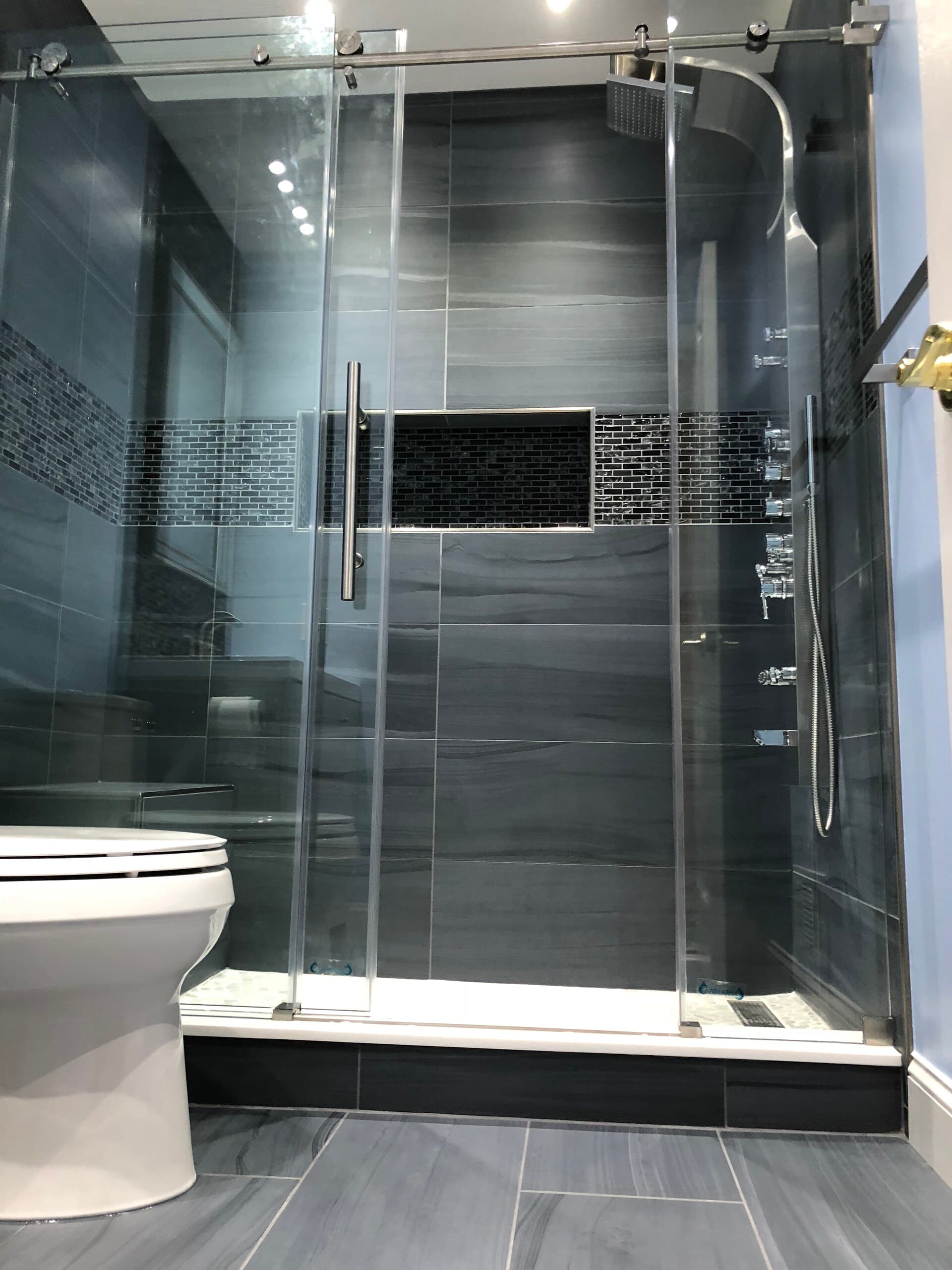 Frameless glass shower with large-format gray tile and a mosaic accent band