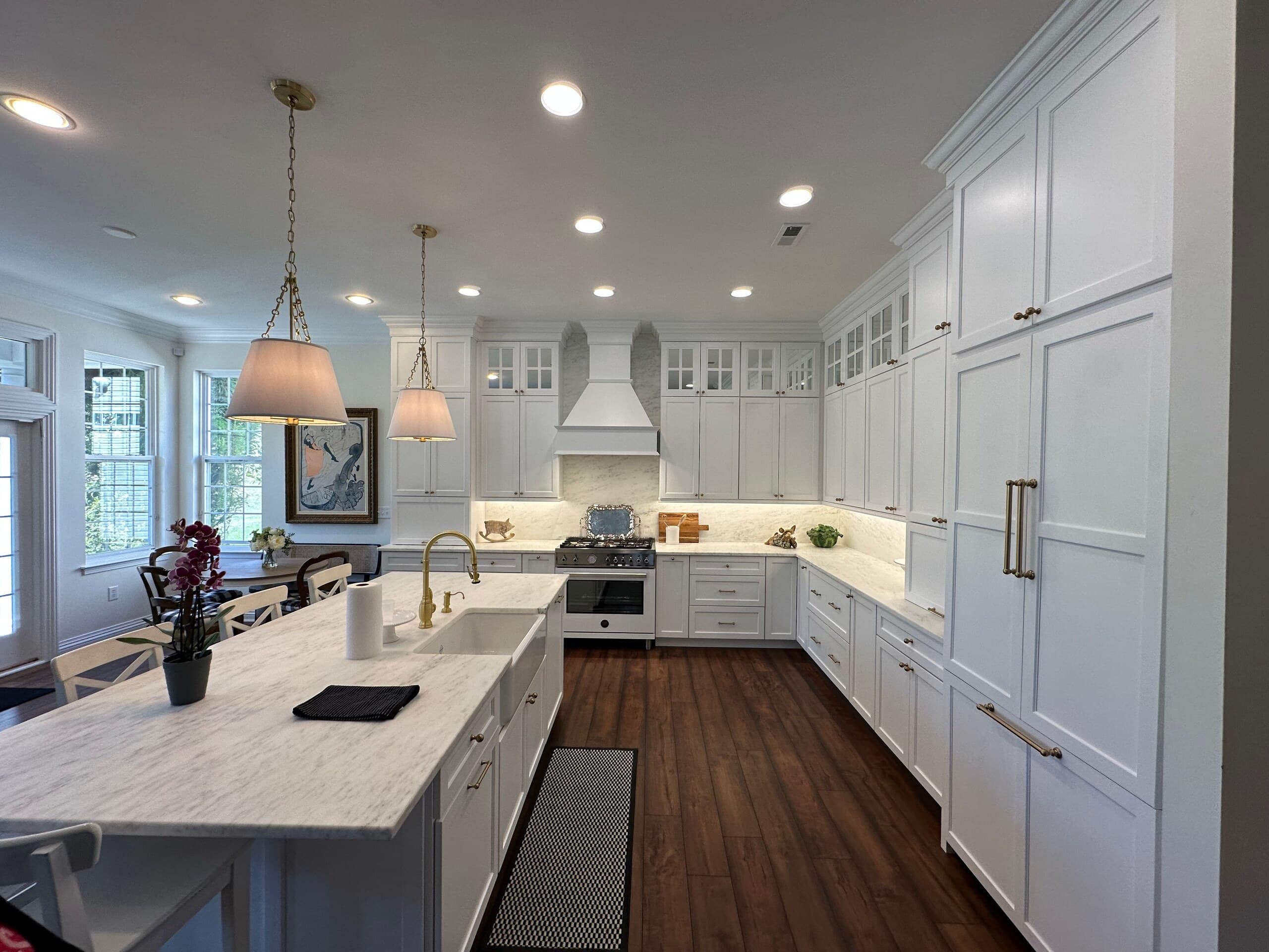 Remodeled white kitchen with a long island, pendant lights and dark wood floors